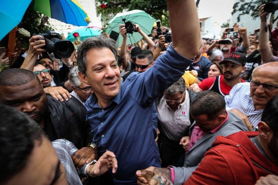 Com camisa azul, Haddad vota e faz sinal de vitória